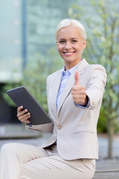 negocios, educación, tecnología, gestos y concepto de personas - mujer de negocios sonriente que trabaja con una tableta que muestra los pulgares hacia arriba en la calle de la ciudad