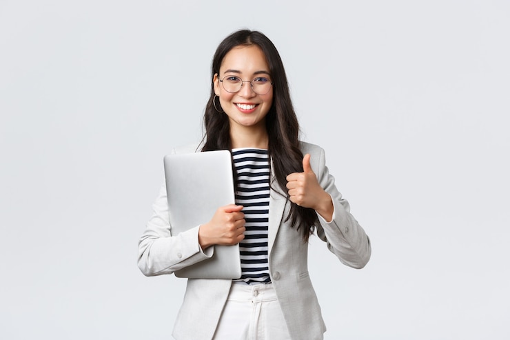 Foto negócios, finanças e emprego, conceito de empresárias de sucesso feminino. terapeuta bonita confiante ou mulher de negócios em um terno branco, segurando o laptop e mostrando o polegar para cima