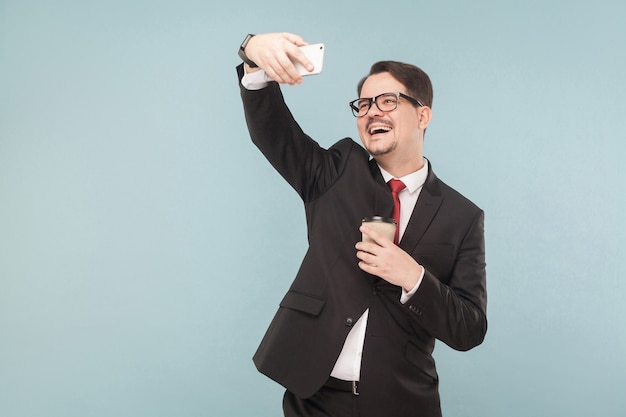 Negocios, gadgets, tecnologías. Hombre de negocios con dientes sonriendo, haciendo fotos. Interior, foto de estudio, aislado sobre fondo azul claro o gris