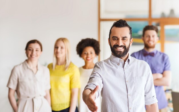 negócios, inicialização, pessoas, gesto e conceito de trabalho em equipe - jovem feliz com saudação de barba por aperto de mão sobre equipe criativa no escritório