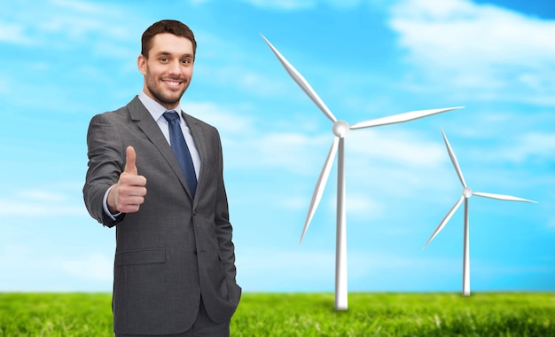 Negócios, inovação, economia de energia e conceito de pessoas - empresário bonito mostrando os polegares sobre moinhos de vento e fundo de céu azul