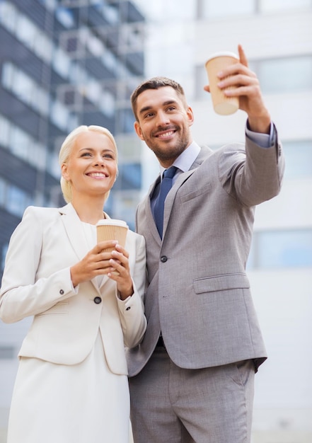 negócios, parceria, bebidas quentes e conceito de pessoas - empresários sorridentes com copos de papel em cima do prédio de escritórios