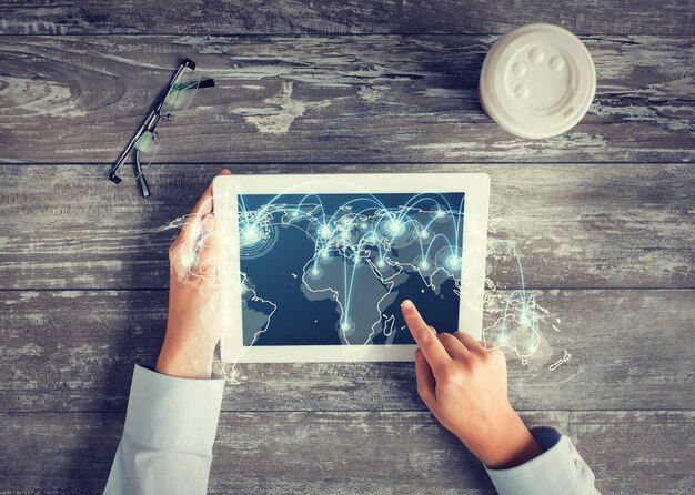 Foto negocios, personas, comunicación internacional, ubicación y concepto de tecnología - cierre de las manos apuntando con el dedo a la pantalla de la computadora de la tableta con el mapa del mundo y la red en la mesa