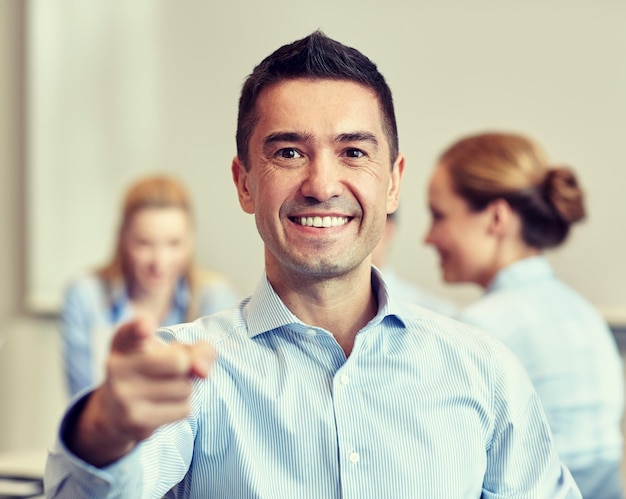negocios, personas, gestos y concepto de trabajo en equipo: un hombre de negocios sonriente señalándote con un grupo de empresarios reunidos en el cargo
