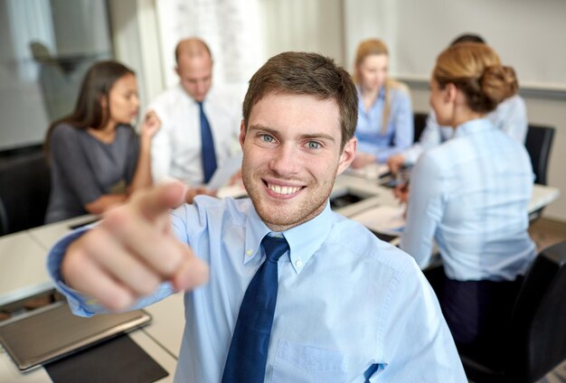 negocios, personas, gestos y concepto de trabajo en equipo: un hombre de negocios sonriente señalándote con un grupo de empresarios reunidos en el cargo