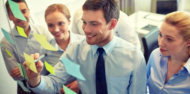 negocios, personas, trabajo en equipo y concepto de planificación - equipo de negocios sonriente con marcador y pegatinas trabajando en la oficina