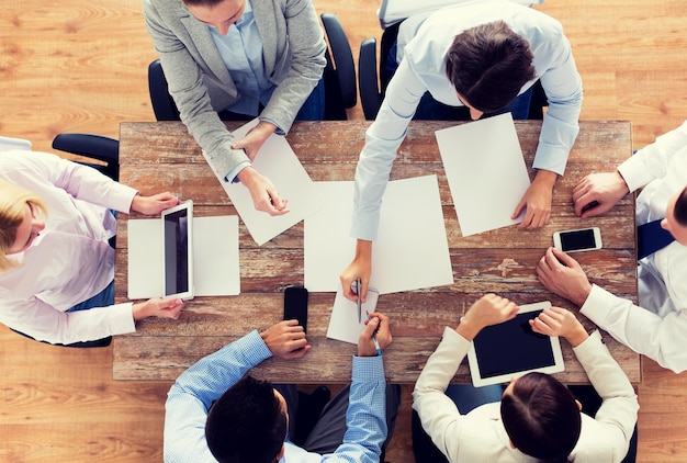 Negócios, pessoas e conceito de trabalho em equipe - close-up da equipe criativa com papéis e gadgets reunidos no escritório