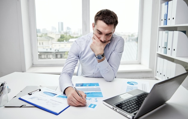 Negócios, pessoas, papelada e conceito de prazo - empresário estressado com papéis e gráficos sentados à mesa no escritório