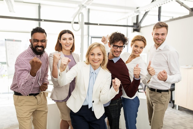 negocios, triunfo, gesto, personas y concepto de trabajo en equipo - equipo creativo feliz mostrando los puños y celebrando la victoria en la oficina