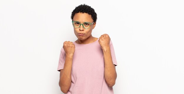 negra jovem afro parecendo confiante, irritada, forte e agressiva, com punhos prontos para lutar em posição de boxe