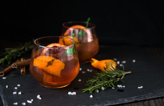 Negroni Cocktail auf Schwarz serviert mit einer Scheibe Orange und Rosmarin.