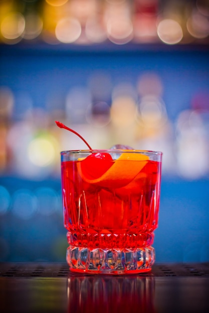 Negroni. cocktail bebida vermelha em frasco de vidro com casca de cereja e laranja com efeito bokeh.