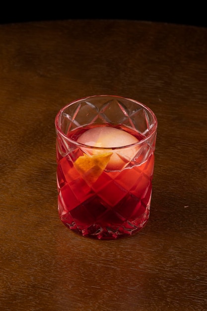 Negroni-Cocktail mit rundem orangefarbenem Eis auf abgewinkeltem Holztisch