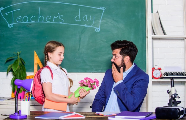 Nehmen Sie dieses Blumengeschenk für den besten Lehrer zurück in die Schule Glücklicher Lehrertag Lehrertag Tochter und Vater mit Blumen Wissenstag 1. September Kleines Schulmädchenkind mit Blumenstrauß