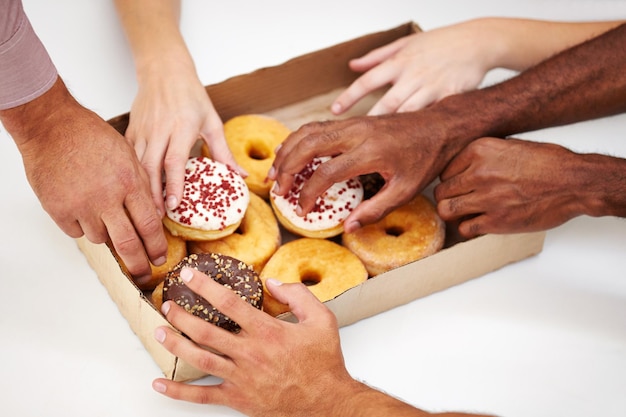 Nehmen Sie einen Bissen Inspiration. Eine Vielzahl von Händen, die nach einem Donut aus einer Schachtel greifen