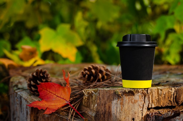 Nehmen Sie schwarze Kaffeetasse mit Deckel auf Stumpf im Herbstparkhintergrund weg. Textfreiraum, verspotten