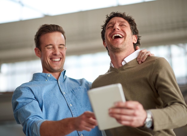 Nehmen Sie sich Zeit für ein gutes altes Lachen Männliche Kollegen, die auf einem digitalen Tablet in ihrem Büro laut über etwas Humorvolles lachen