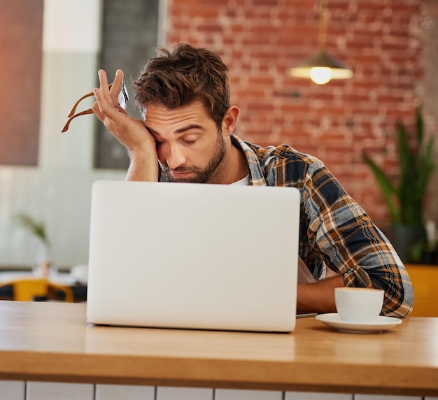 Foto nem mesmo o café pode mantê-lo focado hoje foto de um jovem empresário exausto trabalhando em seu laptop em uma cafeteria