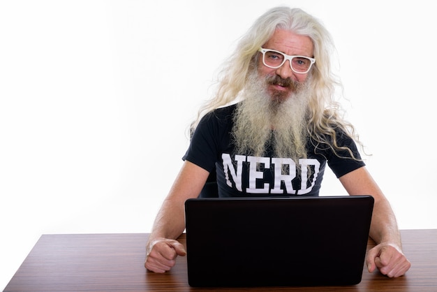 Nerd barbudo sênior usando laptop na mesa de madeira