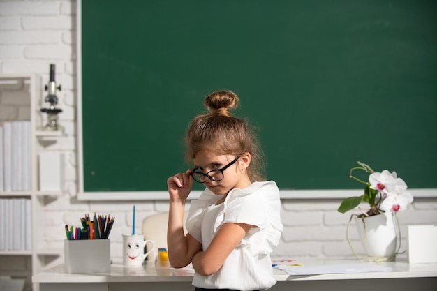 Nerd-Schulmädchen mit Brille auf der Tafel Süße kleine Schulkind-Mädchen studieren in einem Klassenzimmer