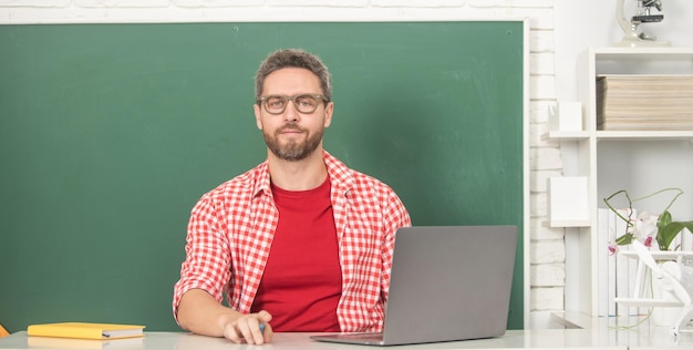 Nerd-Student studiert online. Privatlehrer im Klassenzimmer mit Tafel am PC.