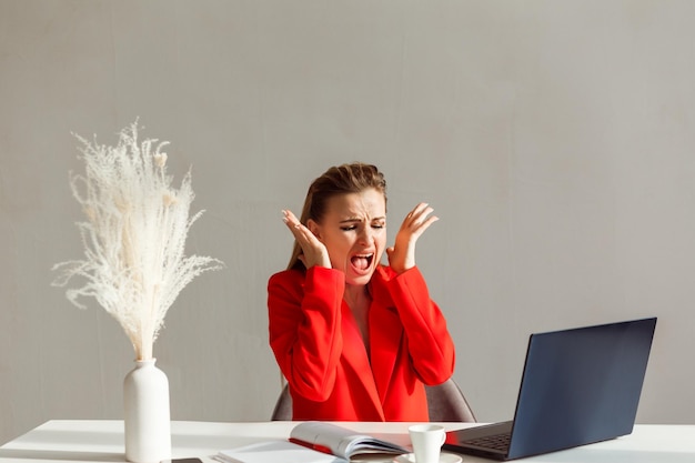 Nervöse Frau im roten Anzug schreit und schaut auf den Laptop-Monitor Frau im Stress bei der Arbeit