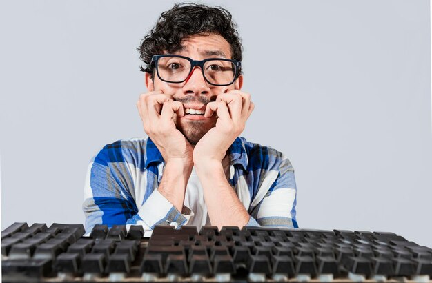 Foto nervoso nerd roendo as unhas na frente do teclado homem preocupado de óculos no teclado do computador jovem rosto preocupado na frente do teclado homem com problemas no computador