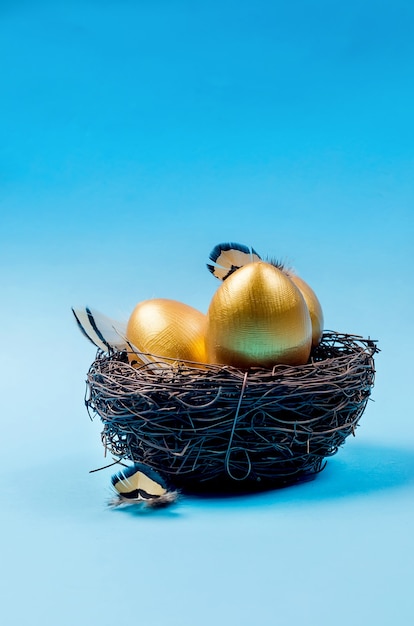 Nest mit goldenen dekorativen Eiern und Federn im Nest auf blauem Grund.