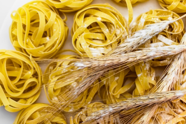 Foto nest-nudeln aus hartweizen, bestreut mit mehl auf weißem hintergrund closeup weizenährchen hausmannskost pasta hintergrund