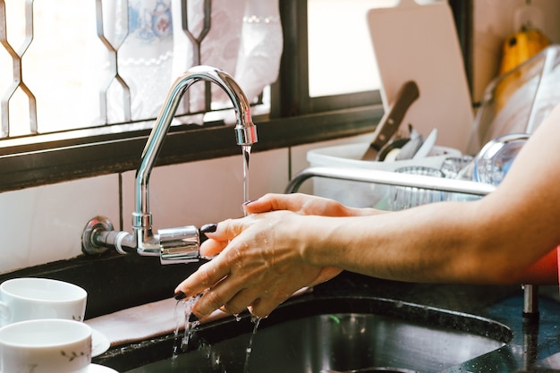 Nesta ilustração fotográfica, uma mulher lava as mãos na pia cheia de pratos sujos.