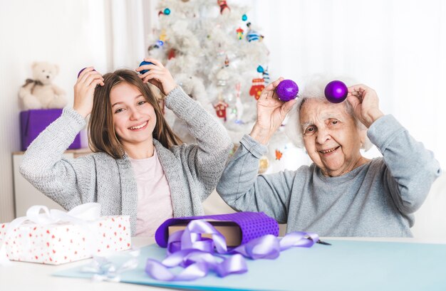 Neta sorridente e vovó brincando com bolas decorativas no Natal