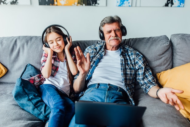 Neto alegre e o avô ouvindo música no tablet digital enquanto está sentado no sofá.