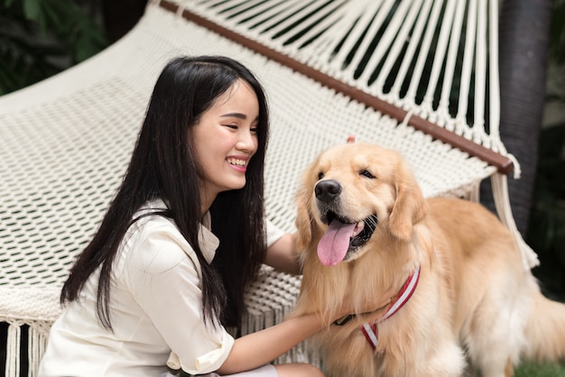 Nette Asiatin, die zu Hause mit ihrem Hund des goldenen Apportierhunds im Garten spielt