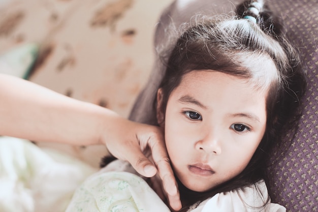 Nette asiatische Kindermädchenkrankheit und Mutterhand berühren ihr Gesicht, um Temperatur mit Liebe und Sorgfalt zu überprüfen