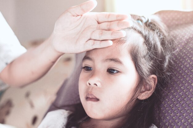 Nette asiatische Kindermädchenkrankheit und Mutterhand berühren ihre Stirn, um Temperatur mit Liebe und Sorgfalt zu überprüfen