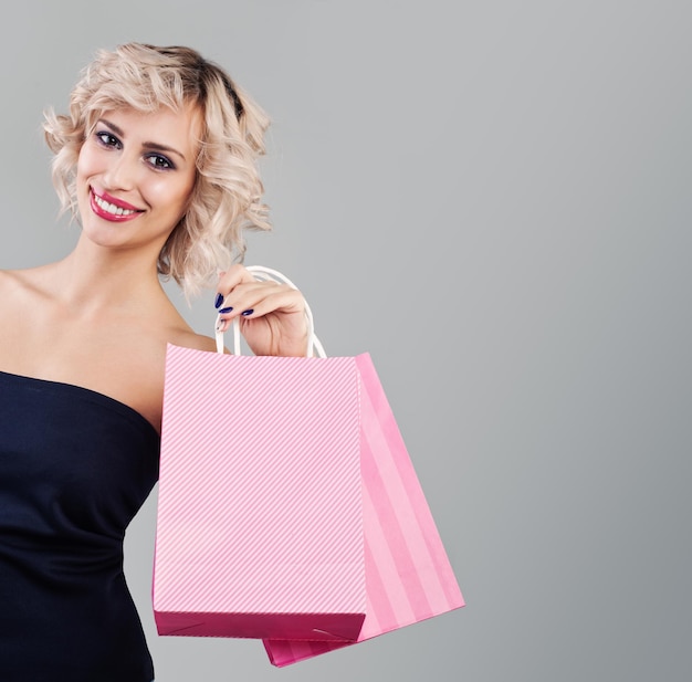 Nette blonde Frau, die Einkaufstaschen auf grauem Hintergrund hält