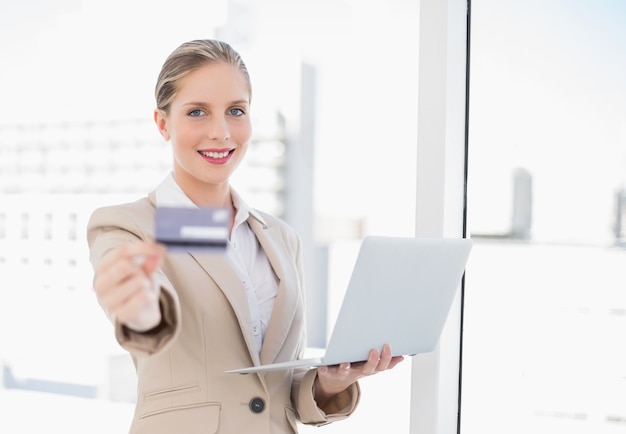 Nette blonde Geschäftsfrau, welche die Kreditkarte hält Laptop zeigt