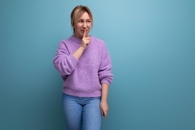 Nette blonde junge Frau im purpurroten Hoodie, die Stillegeste auf blauem Hintergrund mit Kopienraum zeigt