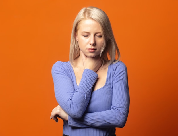 Nette Blondine in blauer Bluse mit Schmerzen im Hals auf einem üppigen orangefarbenen Hintergrund