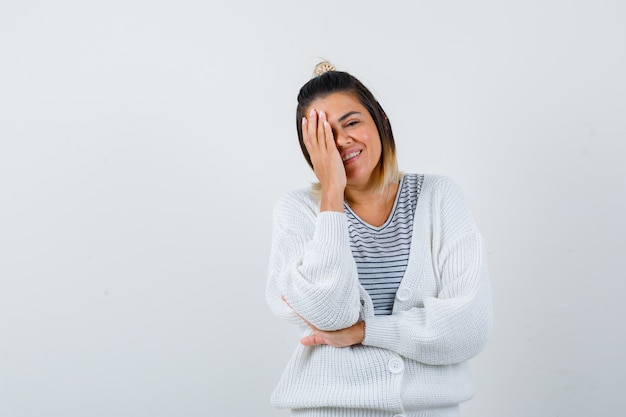 Nette Dame im T-Shirt, Strickjacke, die Hand auf Auge hält und fröhlich schaut