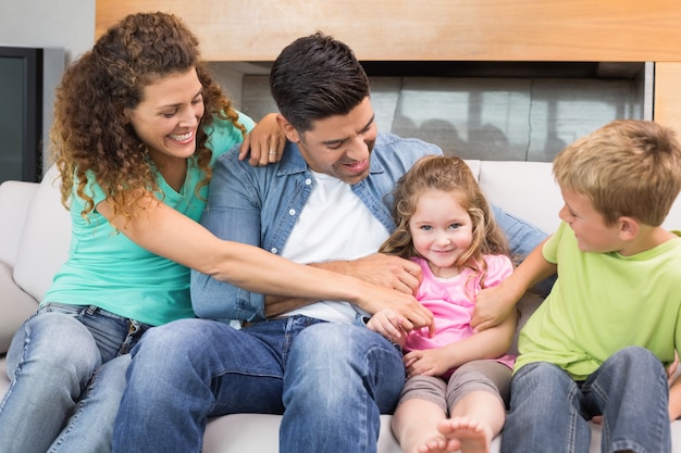 Nette Familie, die kleines Mädchen auf der Couch kitzelt