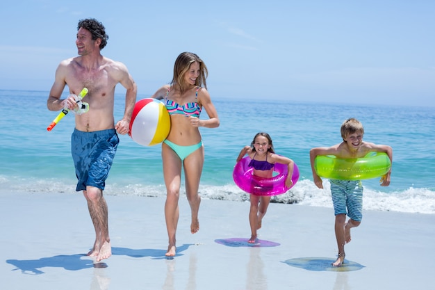 Nette Familie, die mit Schwimmenausrüstung am Seeufer läuft