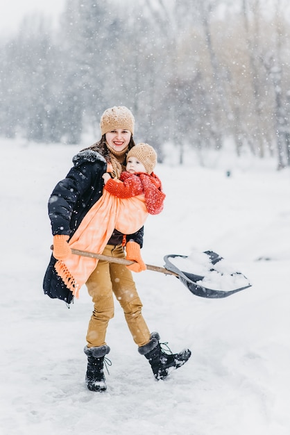 Nette Familie spielt im Park im Winter. Ein Kind in einer Schlinge an ihrer Mutter