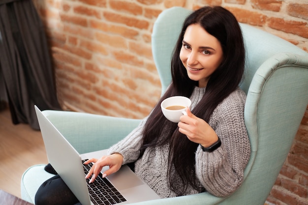 Nette Frau bleiben zu Hause und arbeiten an einem Laptop, der Kaffee trinkt