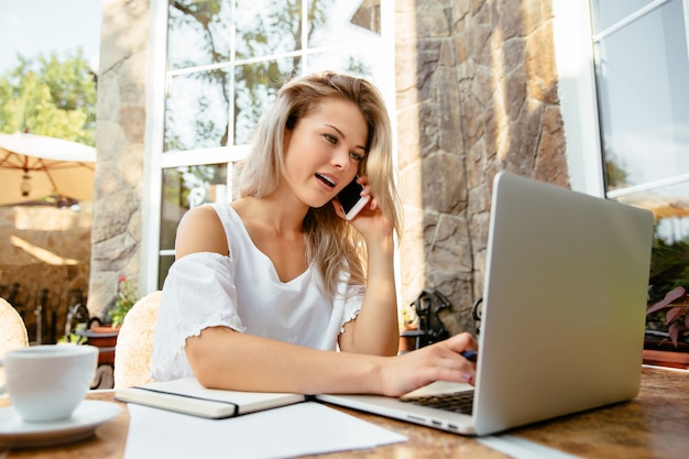 Nette Frau, die am Telefon spricht, während mit Laptop im Freien arbeitet