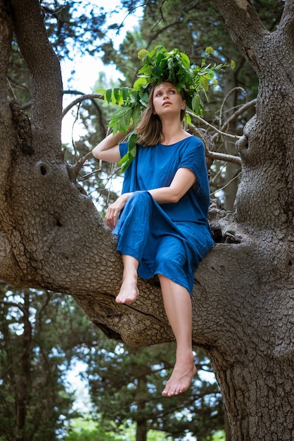 Nette Frau, die auf einem Baum in einem blauen Kleid sitzt