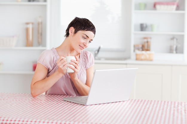 Nette Frau, die mit einem Laptop hält eine Schale arbeitet