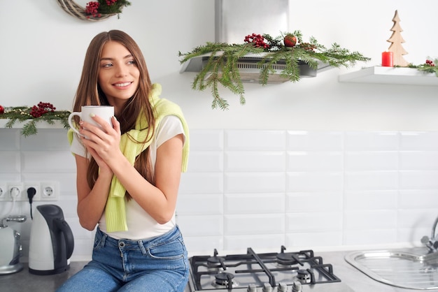 Nette Frau, die zu Hause Kaffee nahe Weihnachtsdekoration trinkt