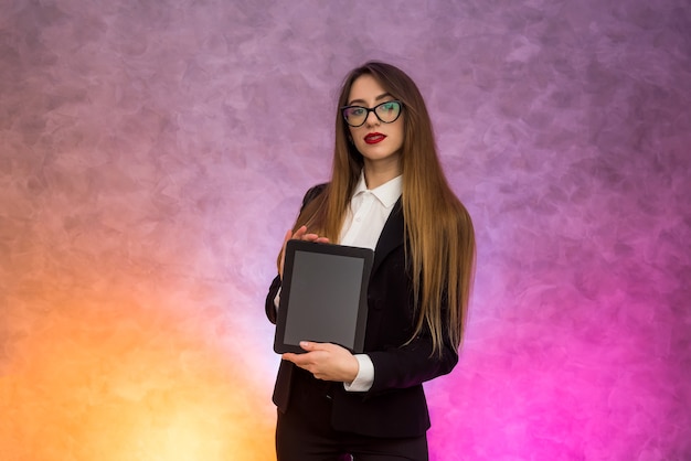 Nette Frau in den Gläsern unter Verwendung der Tablette auf abstrakter Wand