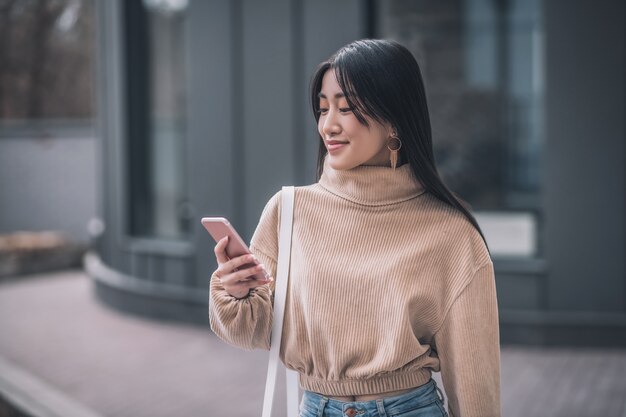 Nette Frau mit einem Telefon. Langhaarige junge asiatische Frau, die ein Smartphone hält